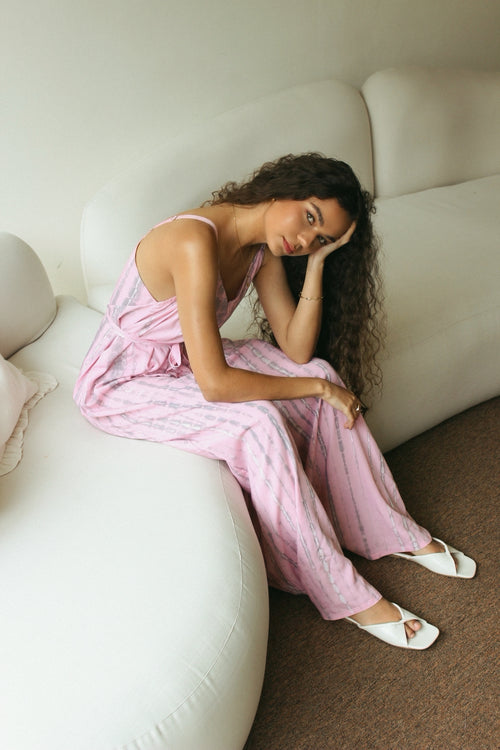 Woman in a bali tie-dye pink jumpsuit sitting on a white couch.